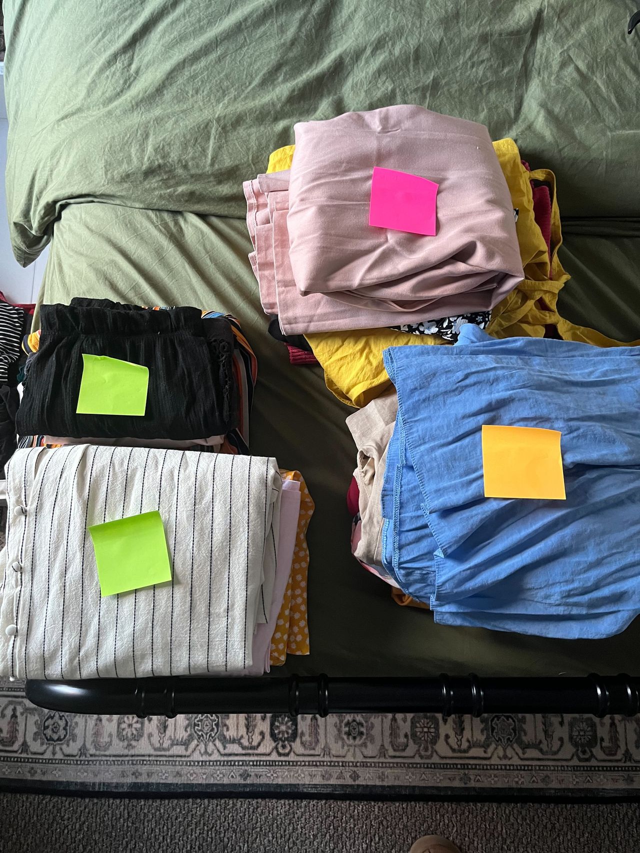 Piles of neatly folded clothes on a green bed with post it note on top