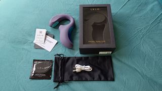 LELO Enigma Double Sonic vibrator out of the box and laid out on a bedspread