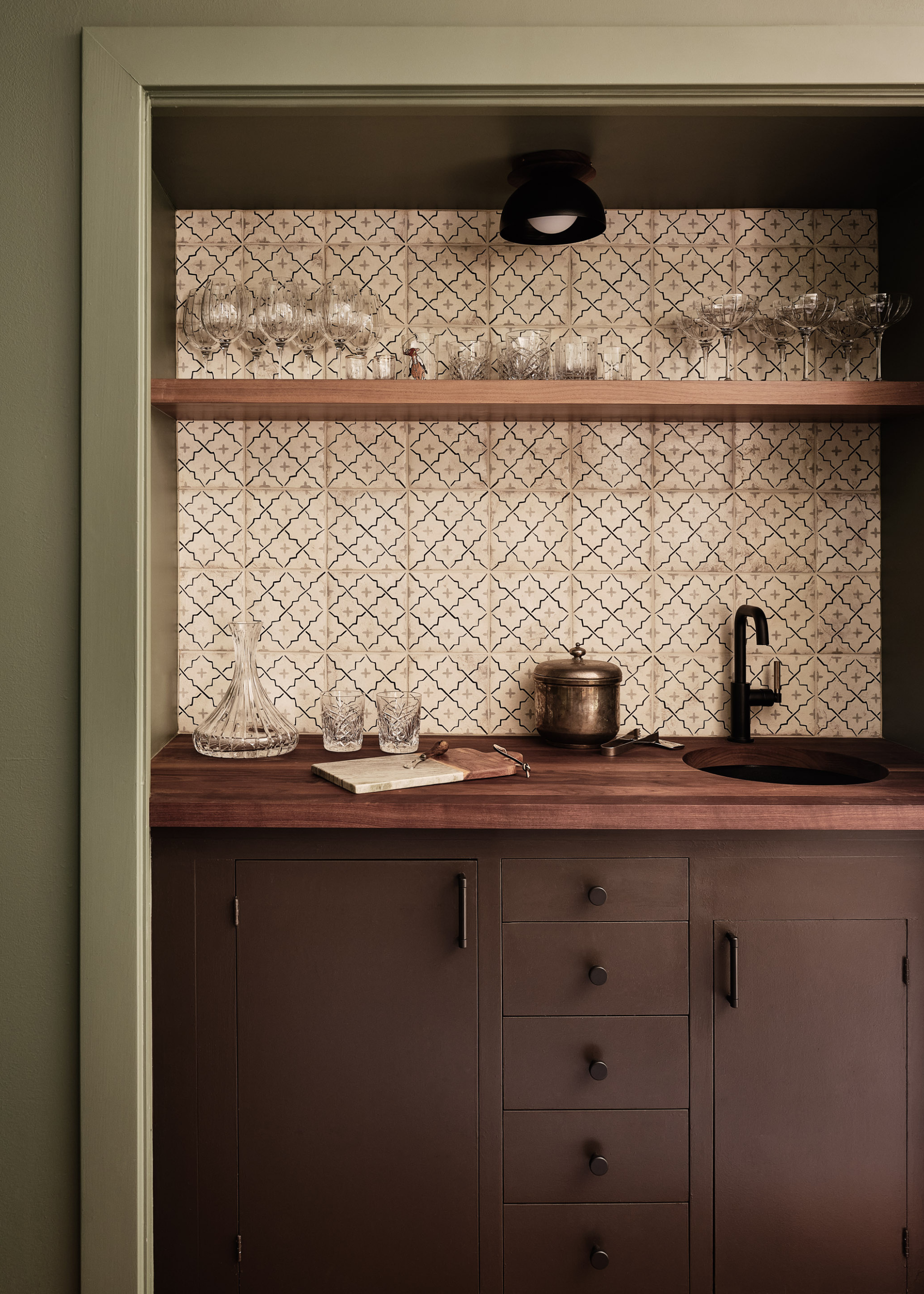 A sage green kitchen with earthy brown cabinets and wooden worktops and patterned tiles for a splashback