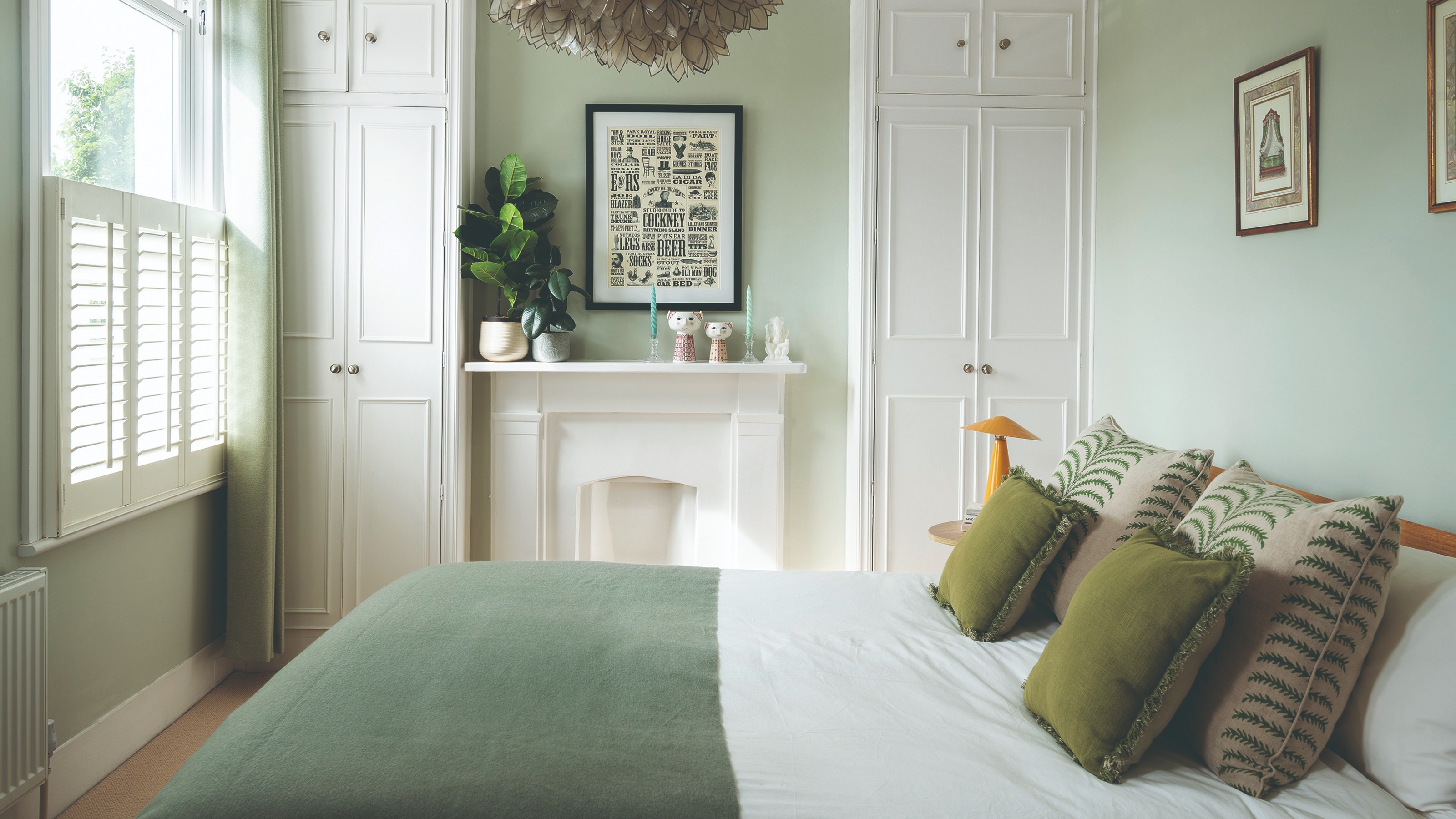 A green bedroom with a white fireplace and built-in wardrobes