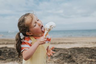 Girl in striped t shirt on a beach eating an ice cream, with ice cream smudge on her nose