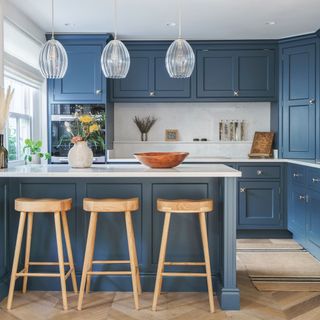 blue kitchen with spotlights in ceiling and three glass pendants above the island with three wooden stools