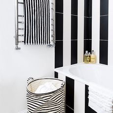A bathroom with black and white tiles, towel and washing basket