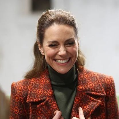 Kate Middleton wearing an orange coat and laughing