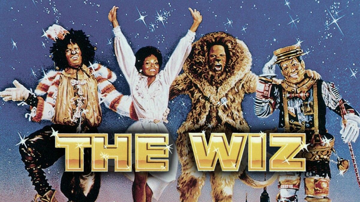 A screenshot of a poster for The Wiz, which shows the main characters standing in front of the movie&#039;s gold colored title