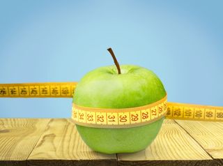 An apple, wound up in a measuring tape, to represent weight loss