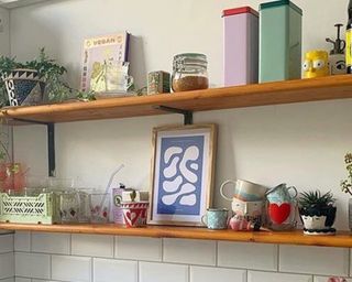 Small kitchen open shelves with colorful accessories including framed art, nested mugs, tall metal tins and trinkets
