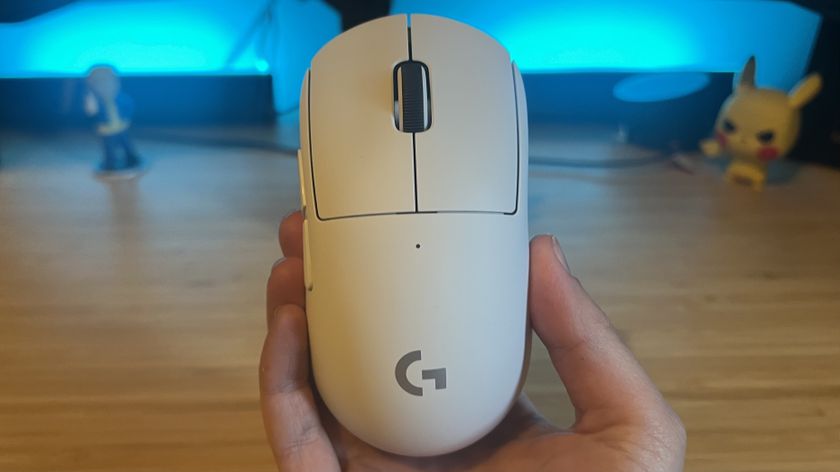 Hand holding Logitech G Pro X Superlight 2c gaming mouse against a wooden desk with blue backlighting