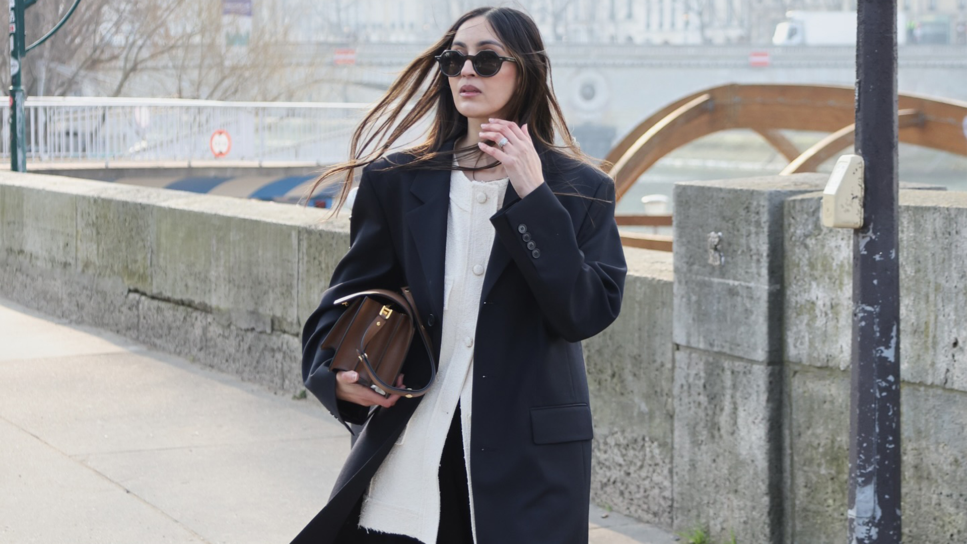 she wears white button down, coat, black pants and shoes while holding a handbag tucked under her arm