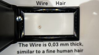 A showcase of a transducer wire next to a human hair, showing them to be the same width