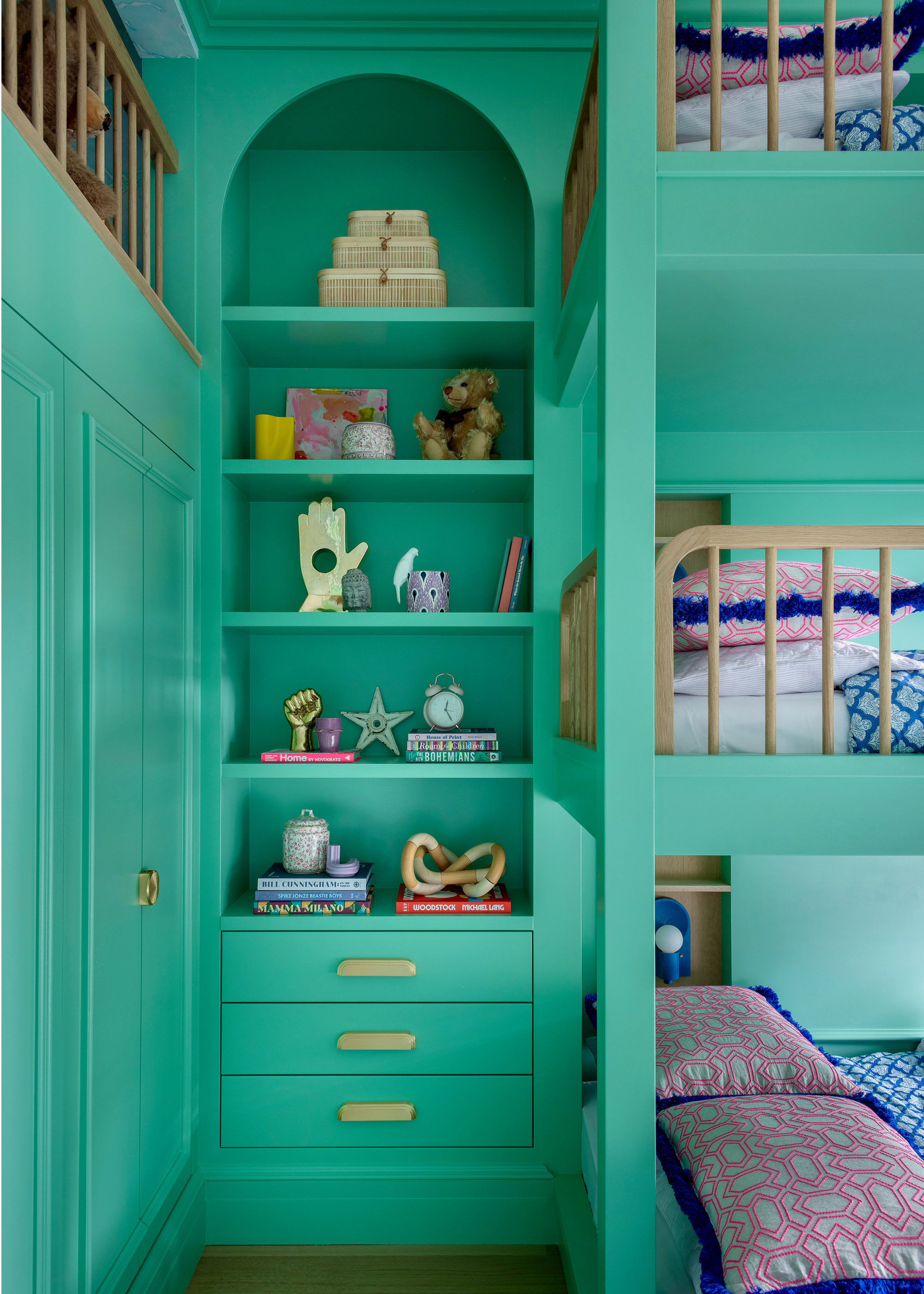 A children's bedroom with a three-tiered bunk bed painted in a vibrant green next to a built-in wardrobe and alcove shelving filled with decorative objects