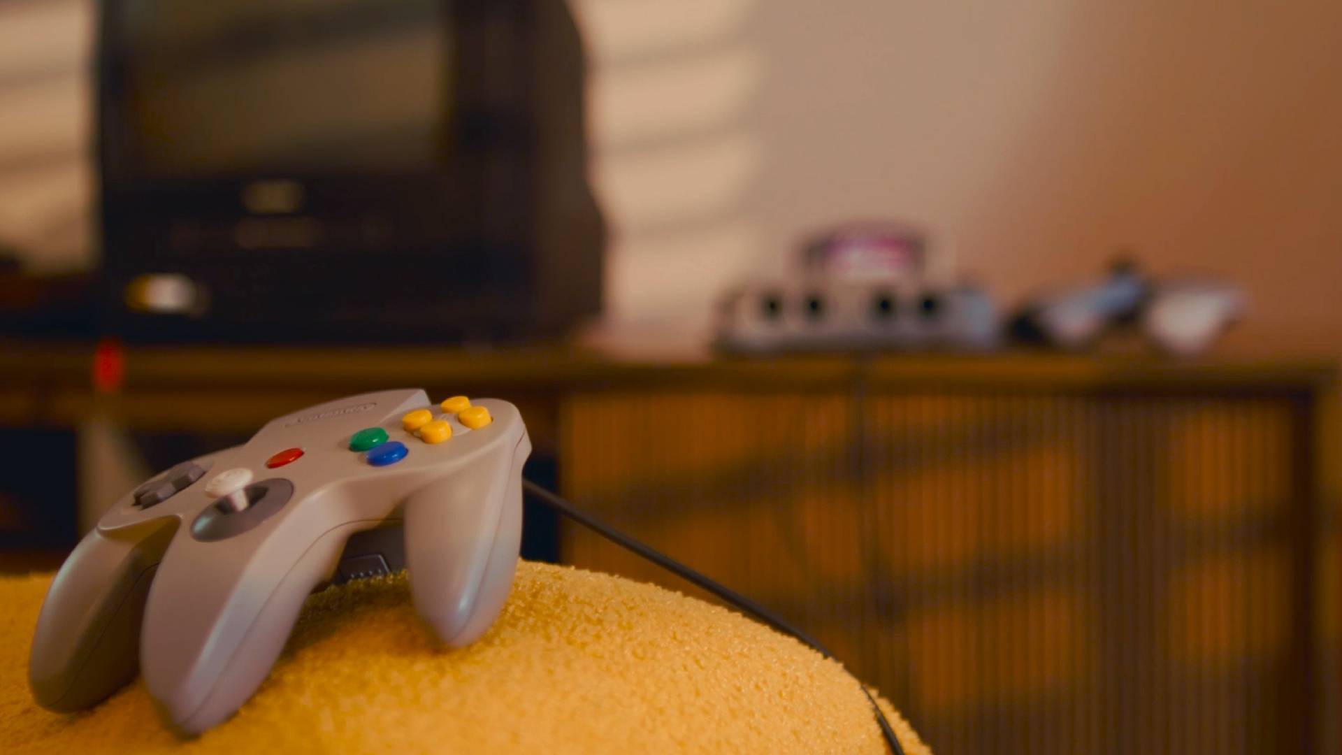 N64 controller with blurred Modretro M64 console in backdrop next to CRT.