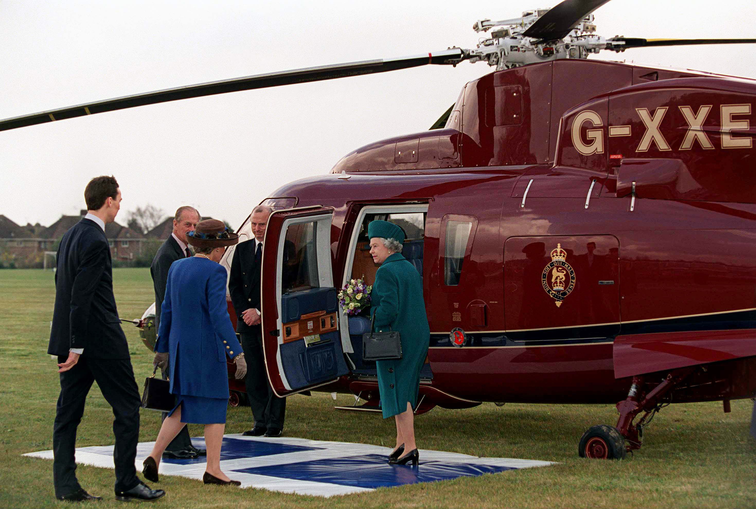 Queen Elizabeth standing in front of a helicopter in a teal coat