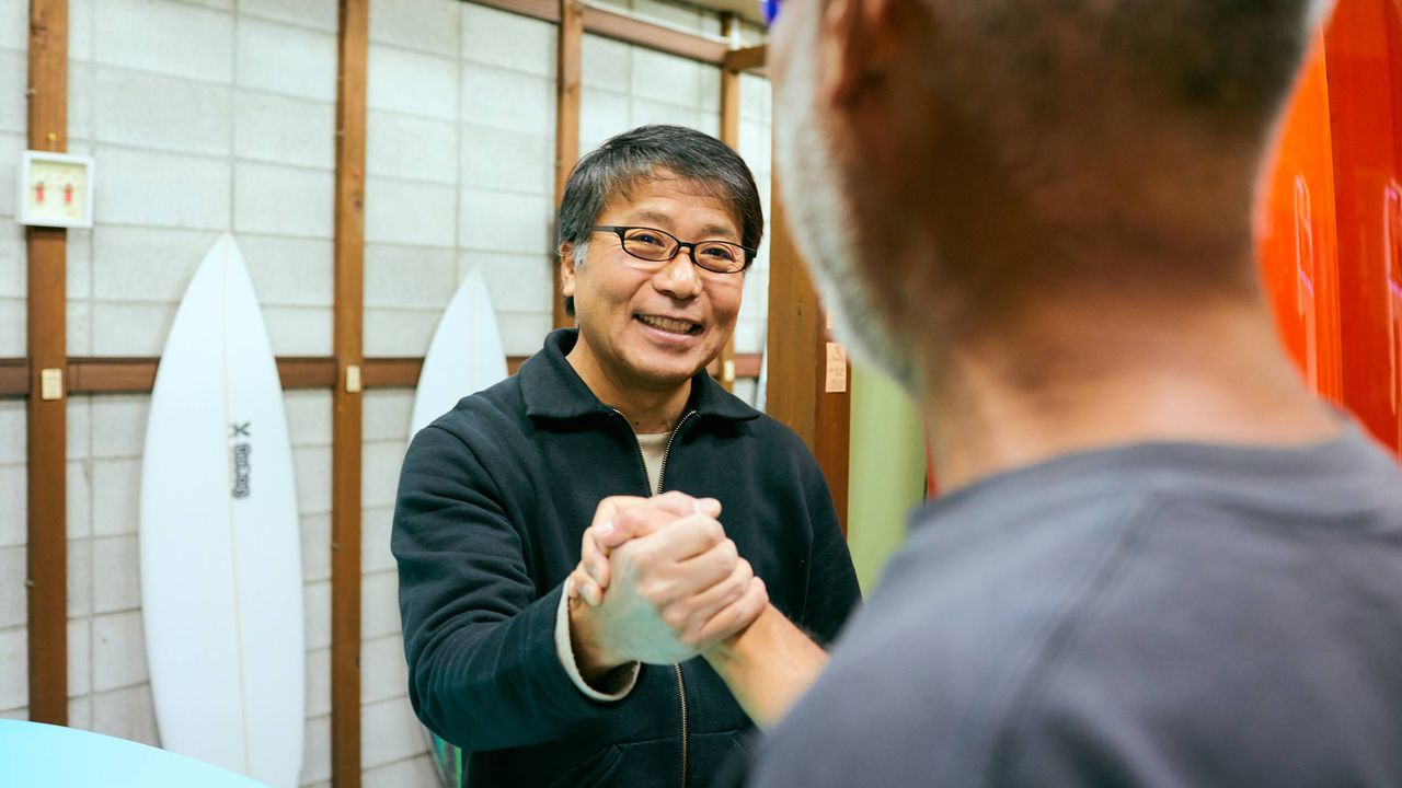 Two senior men shake hands in a surf shop they co-own