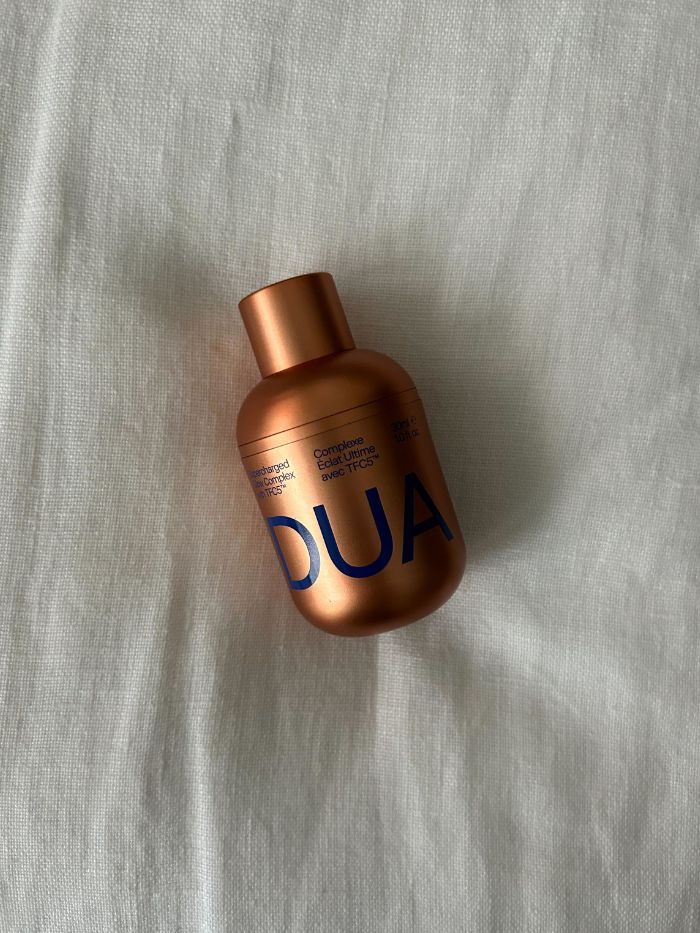 The Dua Lipa x Augustinus Bader skincare serum on a white linen background