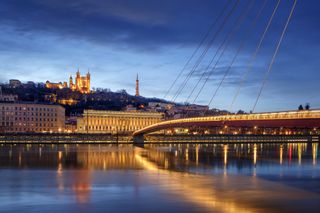 The river front of Lyon, one of the best foodie cities in France. A photograph of the Basilica Notre Dame de Fourviere at night, with the bridge and buildings illuminated