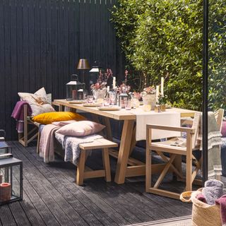 small garden with bench and table, black painted fence, black stained decking, lanterns, seat cushions, throws