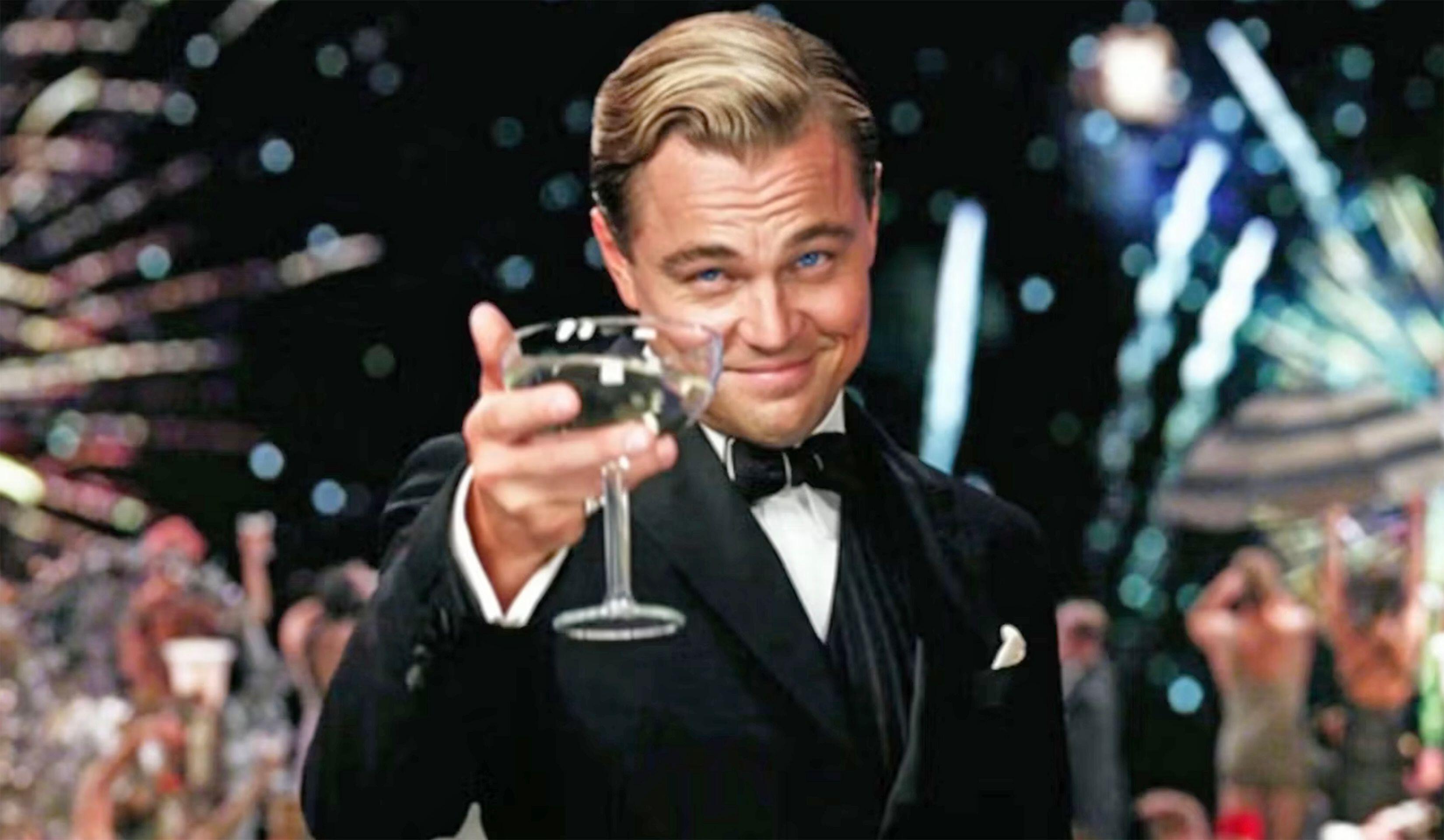 A film still of Leonardo DiCaprio as Jay Gatsby, raising a coupe of Champagne