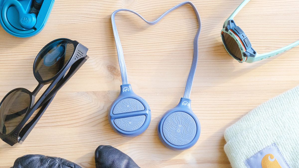 View looking straight down of OutdoorMaster Wireless Ski Helmet Headphones in light blue on a wood table next to a Garmin watch, sunglasses and other outdoor accessories