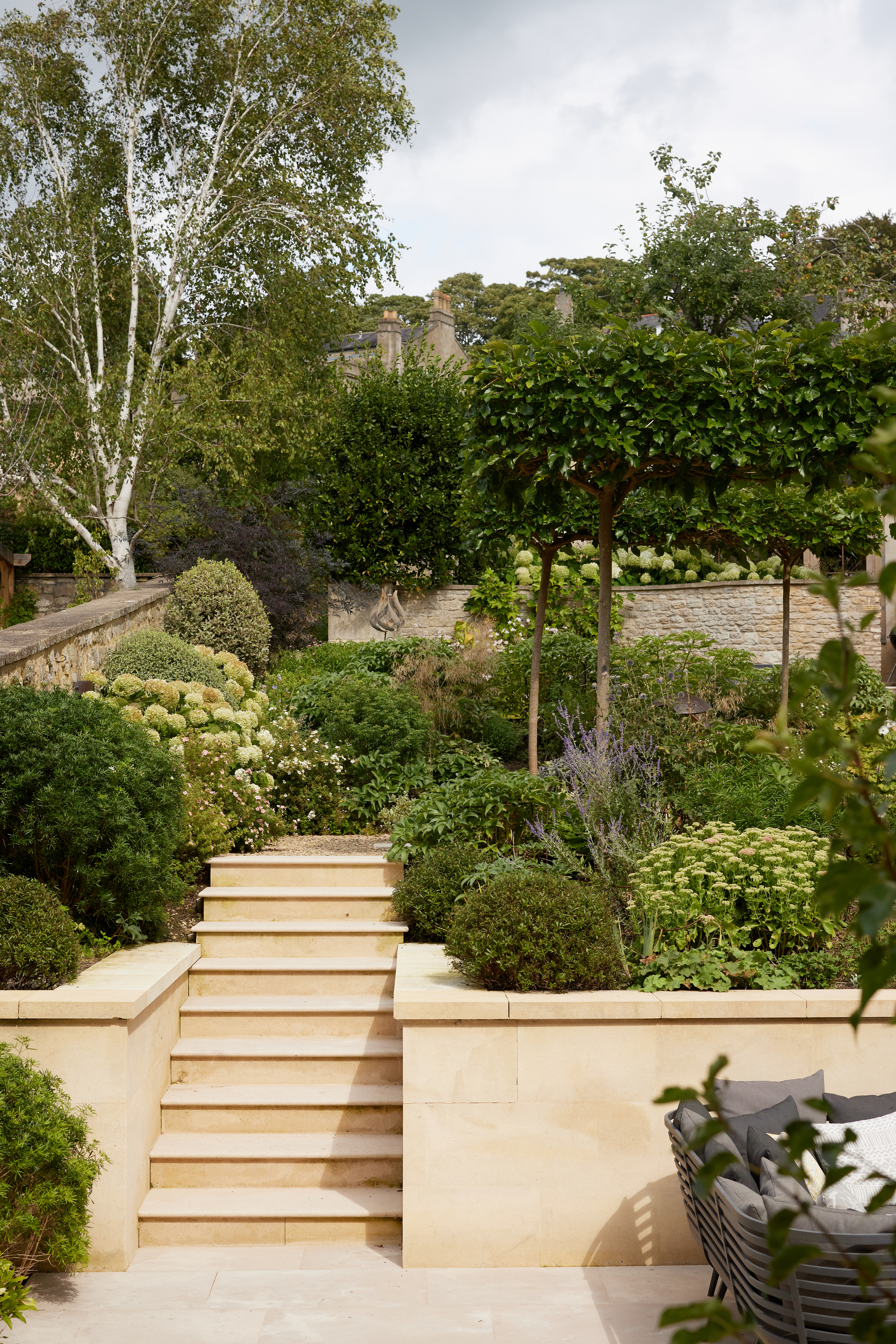 A garden with a set of steps and layered of green foliage, trees and shrubs offering privacy