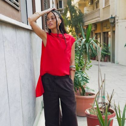 Woman wearing red Whistles top and brown trousers stood outside store
