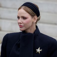 Princess Charlene wearing a black coat and a gold brooch