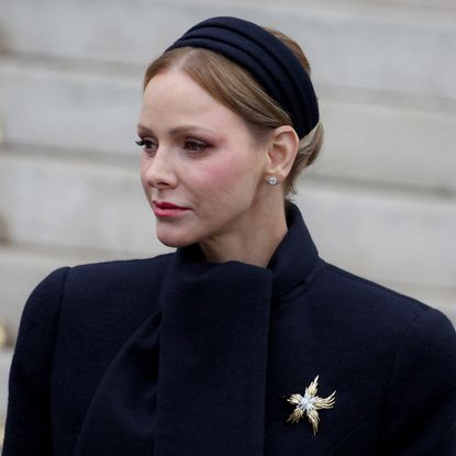 Princess Charlene wearing a black coat and a gold brooch