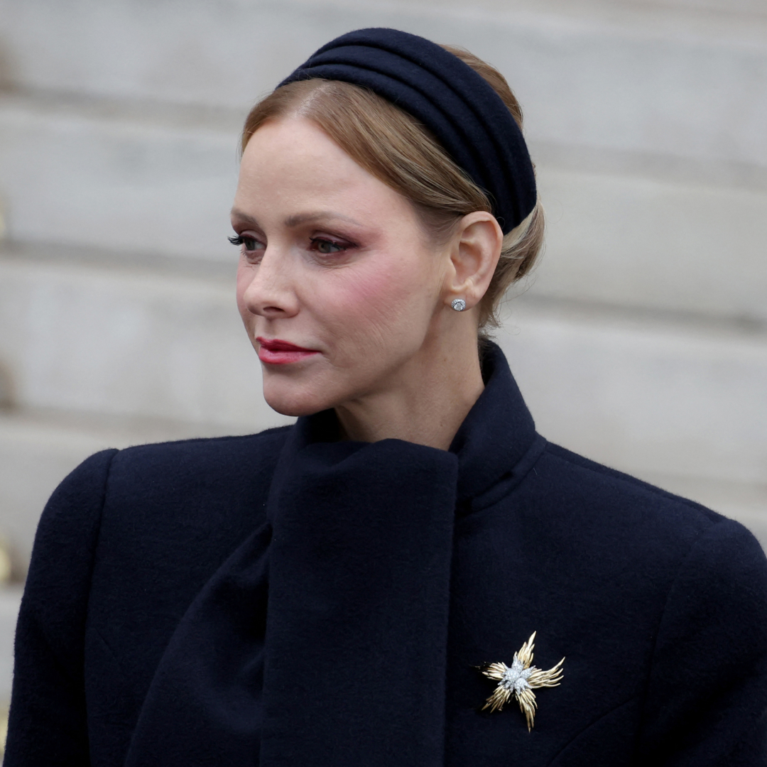 Princess Charlene wearing a black coat and a gold brooch