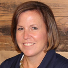 a headshot photo of Kathy Turley, marketing director of Home Clean Heroes: a lady with a short medium brown bob in a navy jacket standing against a wooden wall