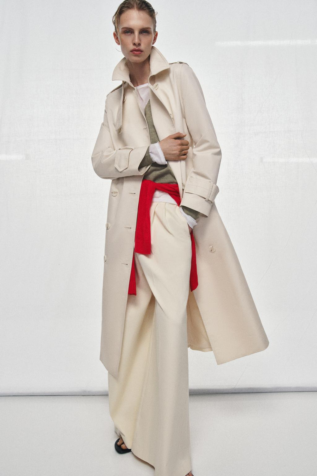 Model wears cream trench coat, green knit, red knit, cream trousers