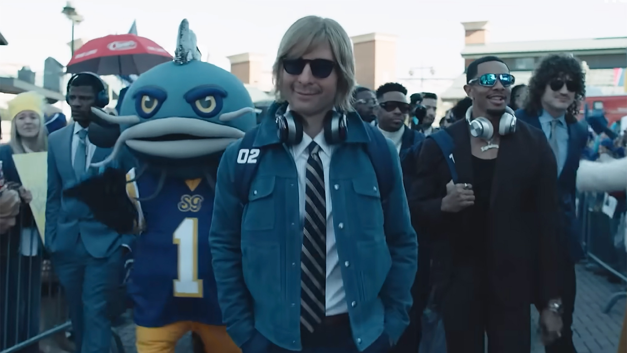 Glen Powell walks into football stadium in Chad Powers prosthetics as his Catfish cohorts walk behind him.