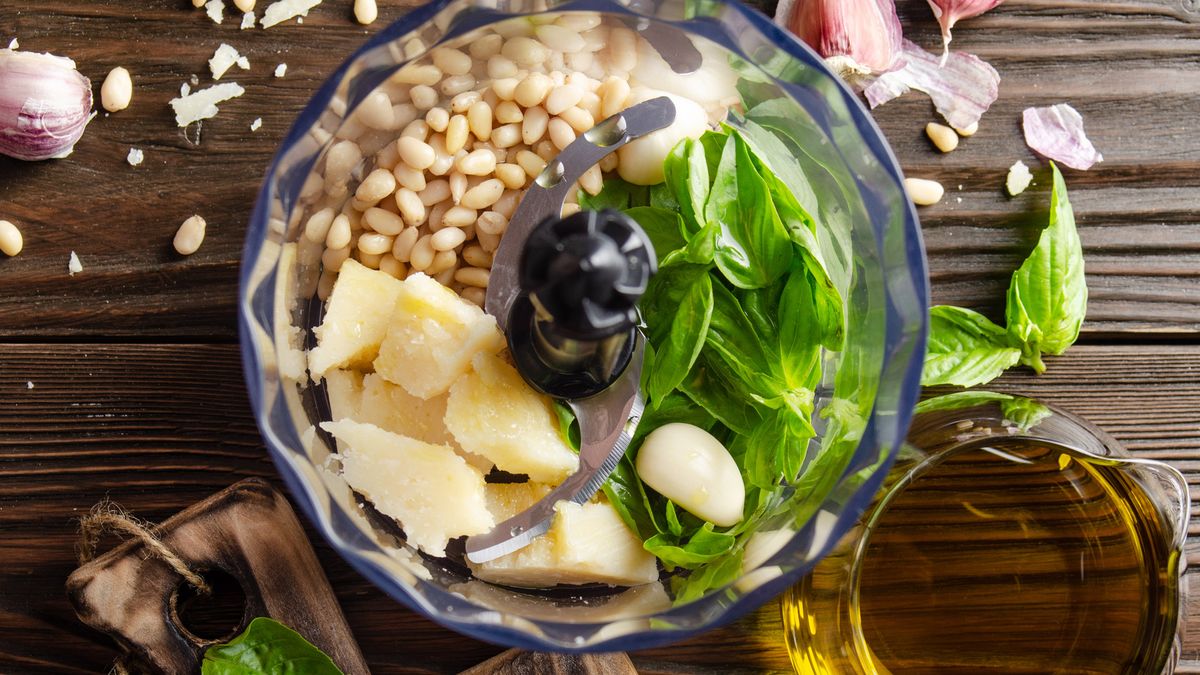 A food processor bowl filled with the ingredients to blend into pesto