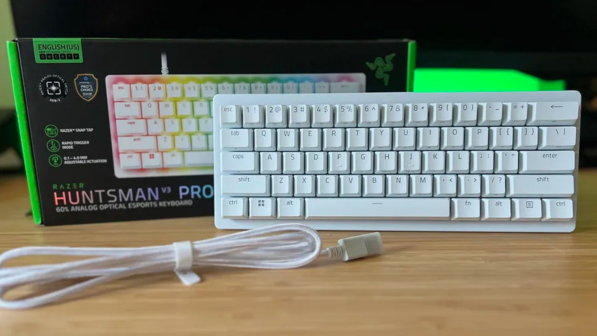 A white Razer Huntsman V3 Pro 60% analog optical esports keyboard sits in front of its black product box on a wooden desk with a coiled white cable.