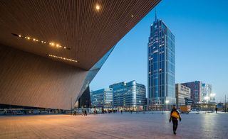 View looking out from the Rotterdam Central Station entrance, wooden archway entrance, ceiling lights, view of high buildings and city landscape, visitors, blue dusk sky