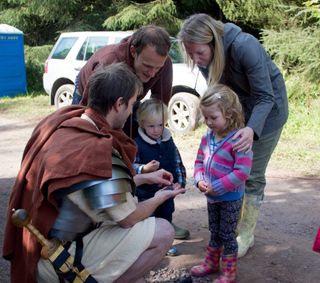Here, a reenactor named Quintus shows pieces of Roman pottery to visitors at an Open Day at the Burnswark Hill site.