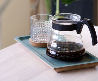 A glass drip coffee maker carafe on a tray with a coffee glass