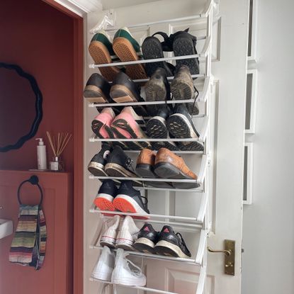 white door with a white shelving rack holding shoes and trainers with a glimpse of a red bathroom behind