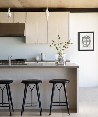 Kitchen with island with pendant lights over, bar stools and range and wall cabinets beyond