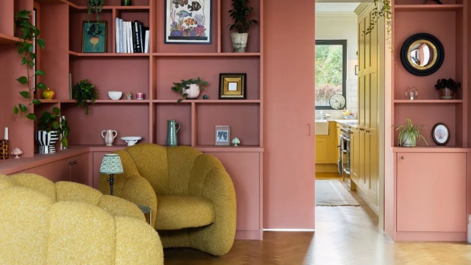 A pink room with books stored in cubby holes around the room and two yellow armchairs in front of them