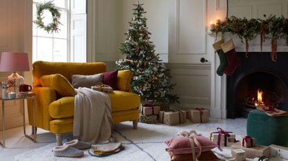 A christmas treein the corner of a living room, a yellow arm chair in front of it 