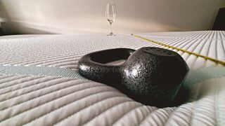 A closeup of a 10lb kettlebell roughly two feet away from an empty wine glass (as measured by the tape on the right) during a motion isolation test for the Tempur-Pedic Tempur-Adapt Mattress