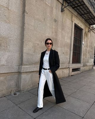 fashion influencer @annabelrosendahl wearing white jeans, a white T-shirt, black coat, black loafers, and black leather belt