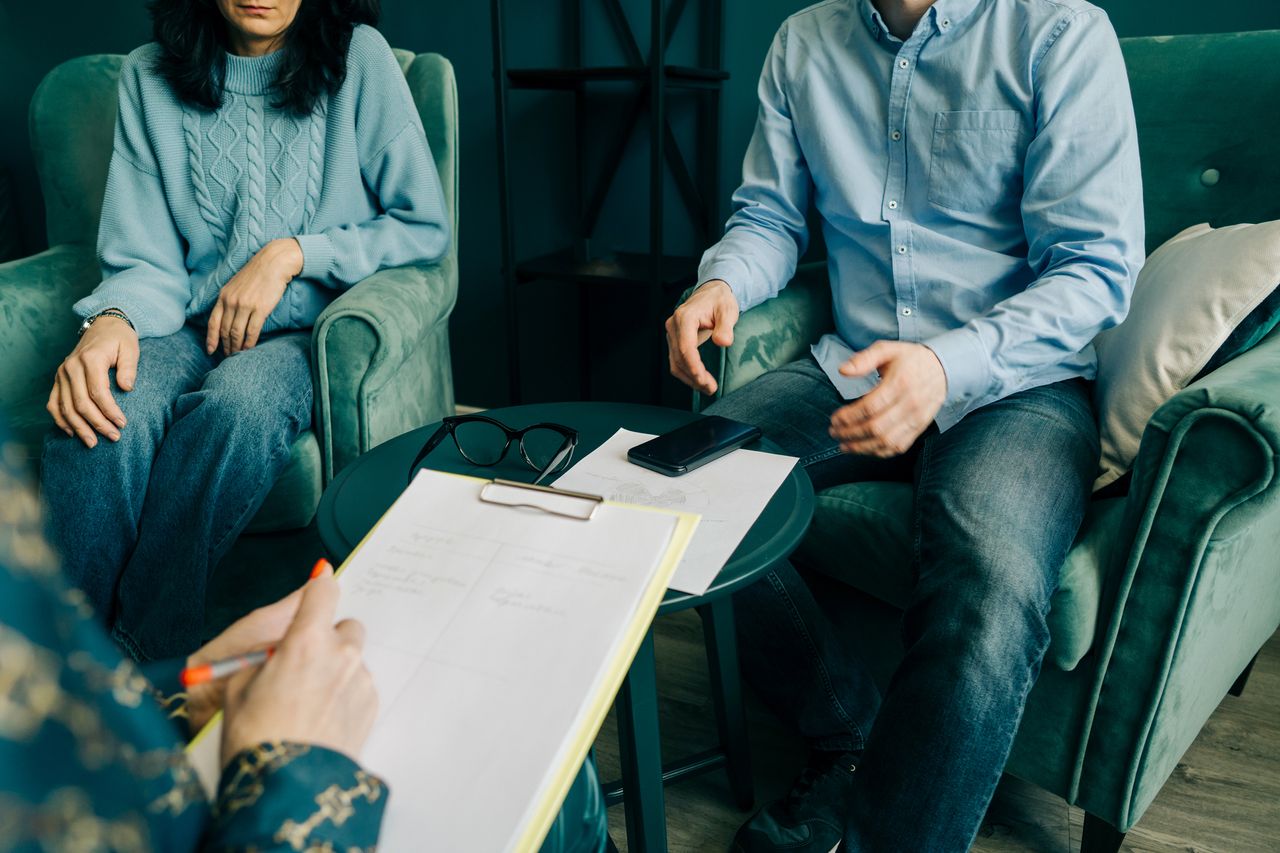 Couple sitting on sofa talking to therapist with paper in her hand