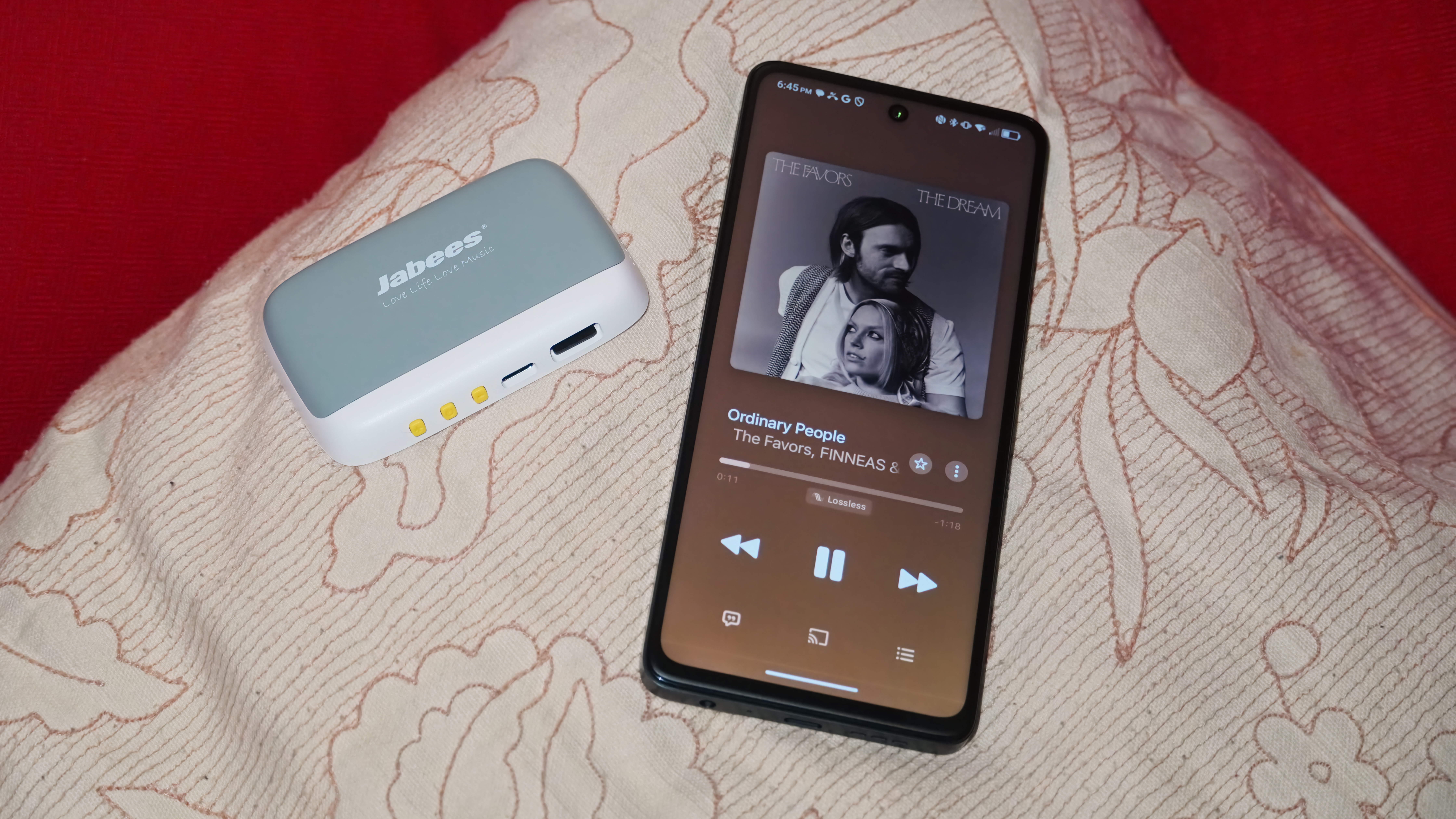 Το Jabees Peace Pillow Speaker σε ένα μαξιλάρι δίπλα σε ένα smartphone.