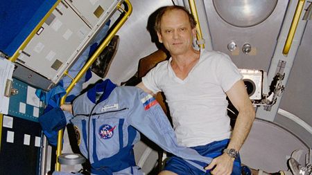 Astronaut Norman E. Thagard floats in the Space Shuttle Atlantis holding the flight suit he wore on Russia's Mir Space Station during the Mir-18 mission in 1995. This photo was taken on July 7, 1995, the last day of his four-month mission.