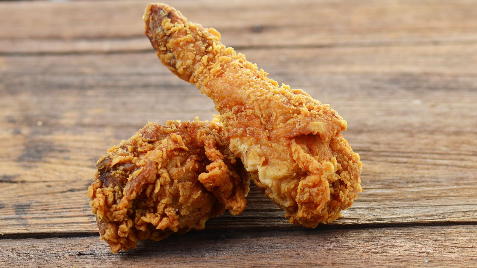 Two crispy pieces of fried chicken on a wooden platter