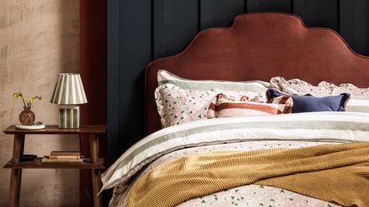 A bedroom with layered bedding on the bed and the M&amp;S Ollie table lamp on the bedside table