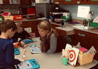 A kindergarten teacher does small group instruction as her Nebula projects her iPad in the background