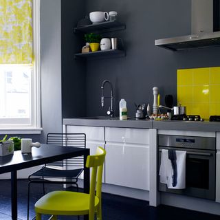 grey kitchen with yellow tiled backsplash behind hob and black dining table