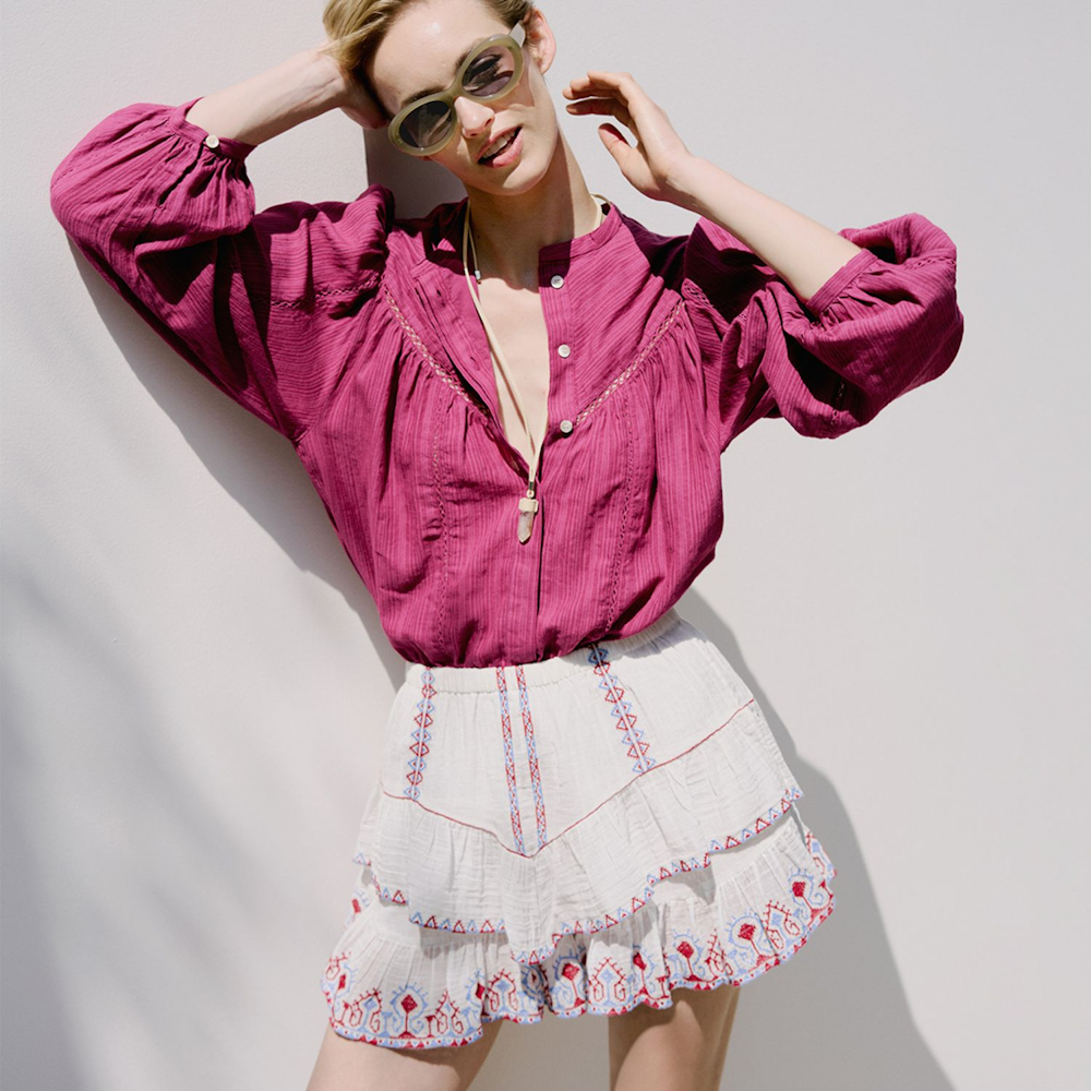 A woman posing against a white background in a pink shirt and a white gypsy style skirt from THE OUTNET